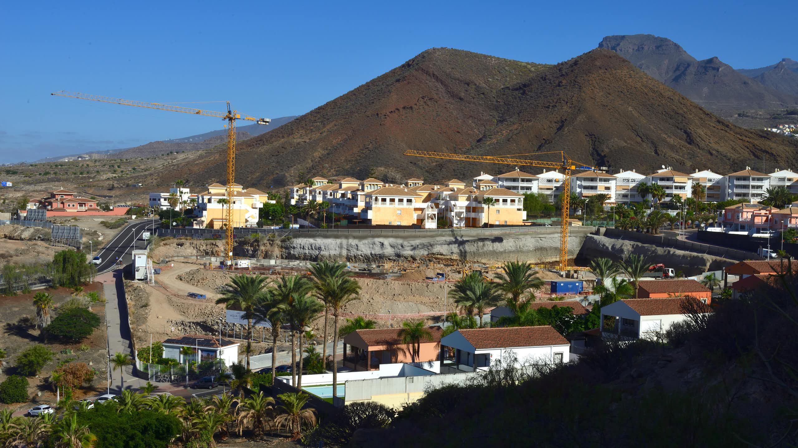 Viviendas en construcción con grúas en un paisaje volcánico.