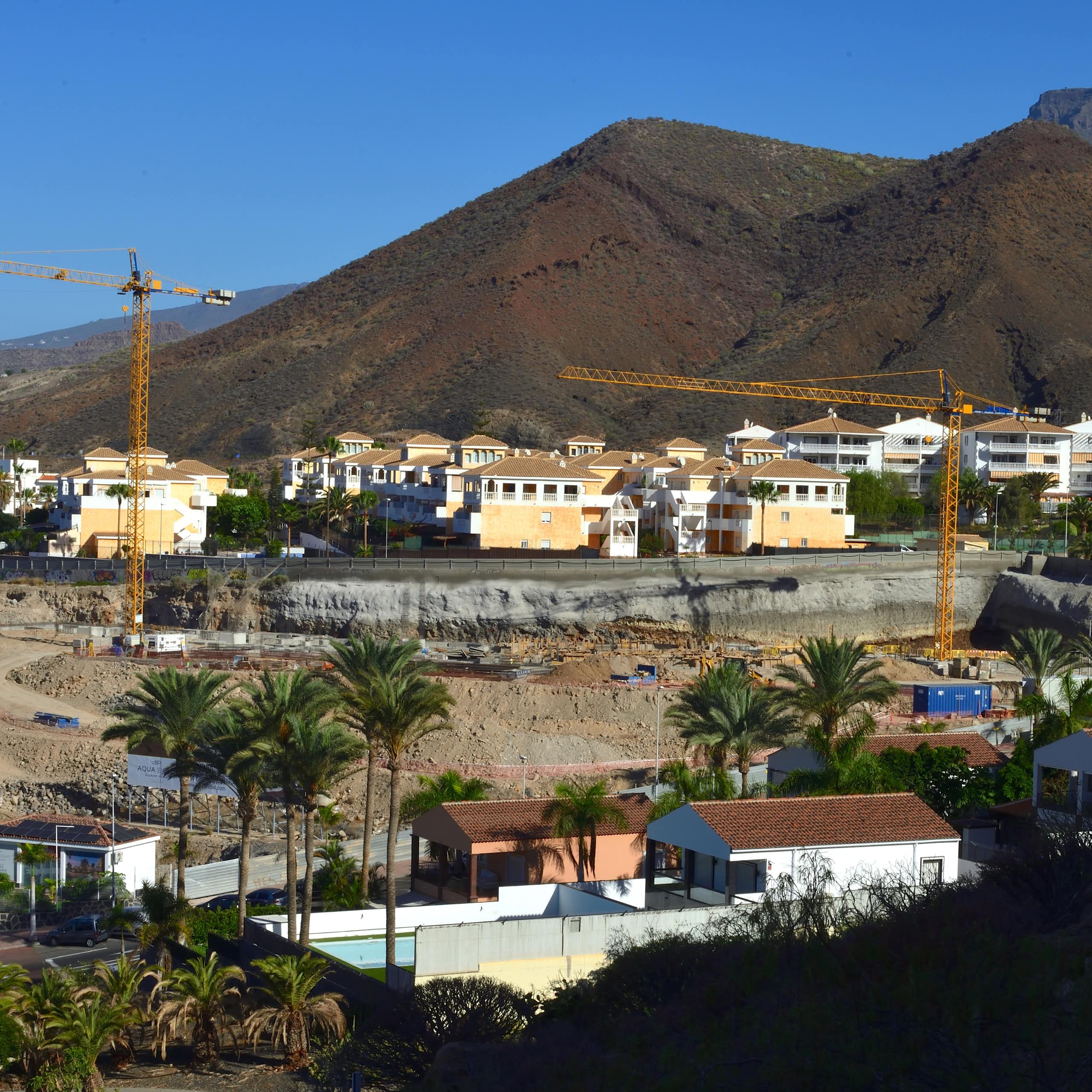 Viviendas en construcción con grúas en un paisaje volcánico.