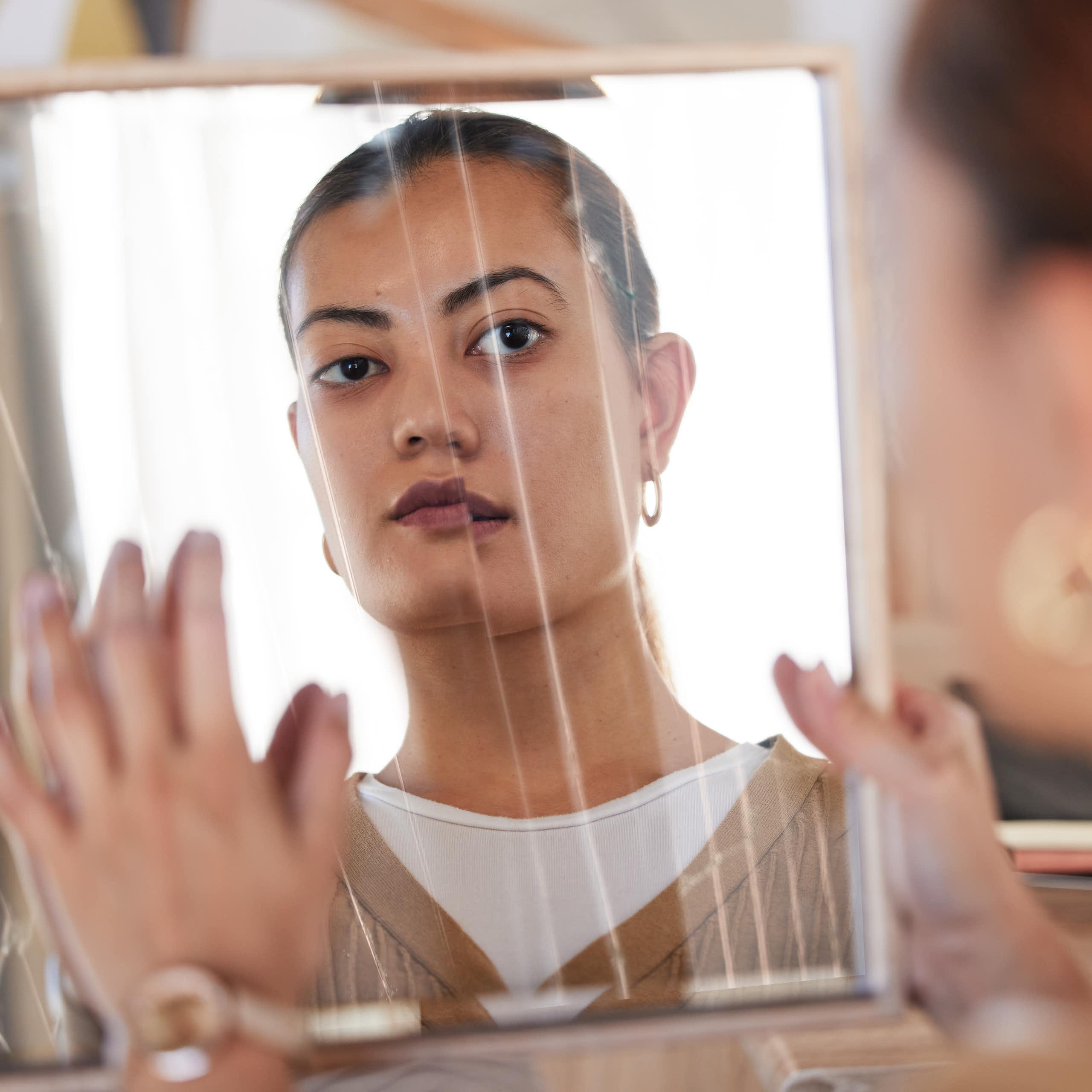 A young woman looking somberly into a broken mirror