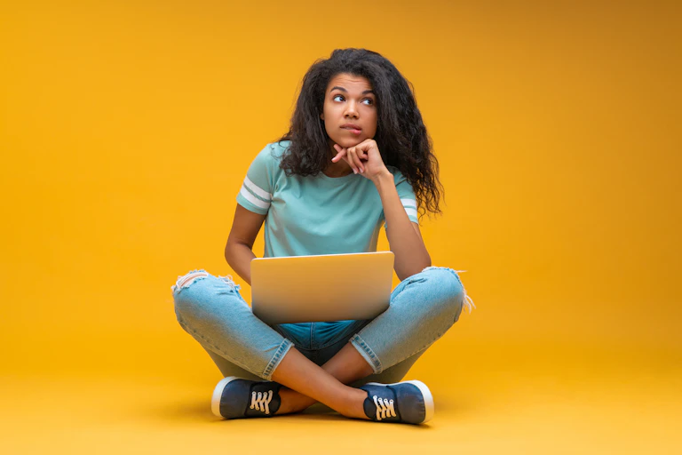Girl with laptop looking pensive on yellow background
