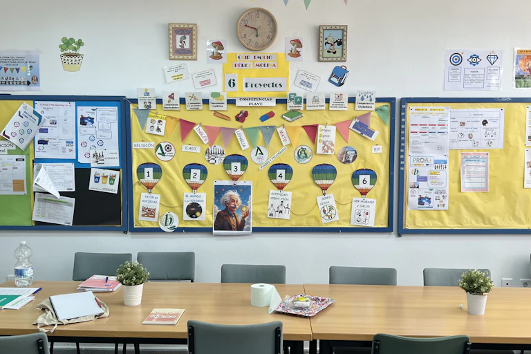 Aula escolar con mesas y sillas vacías con carteles de trabajos sobre Einstein en la pared.