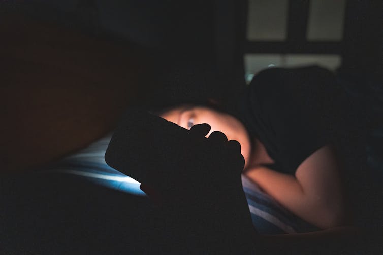 A woman staring at her cellphone while lying in the dark.