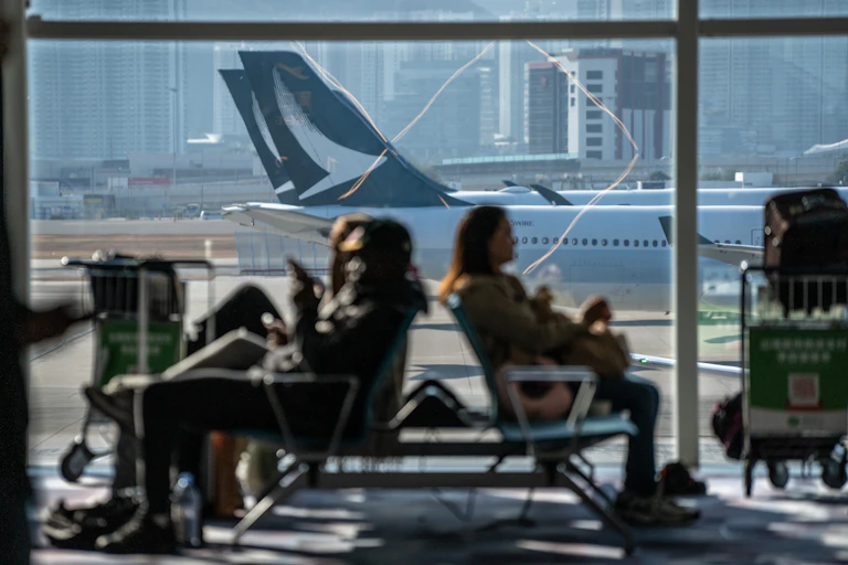 people sitting in a waiting area with jetliners visible through a large window
