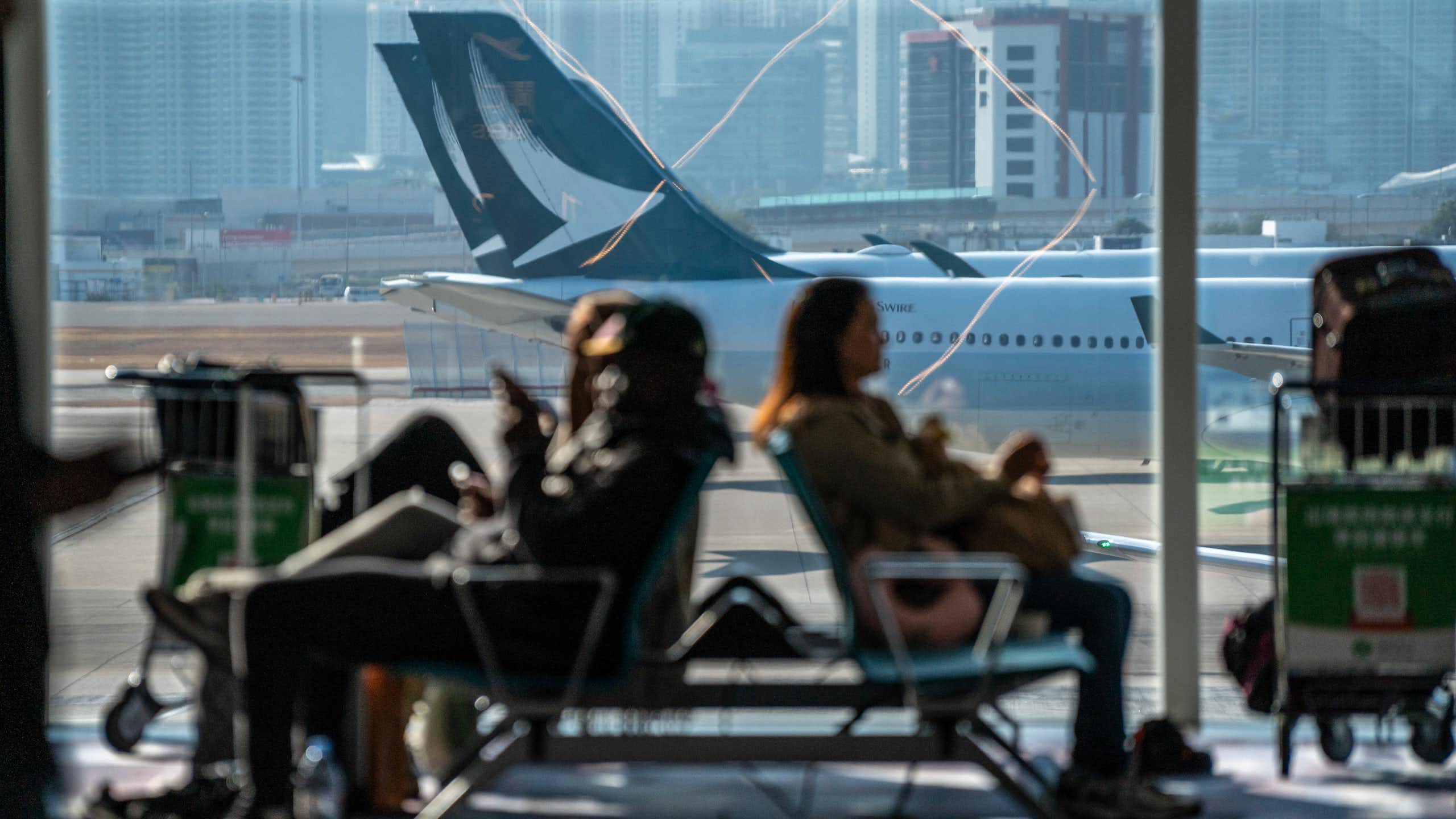 people sitting in a waiting area with jetliners visible through a large window