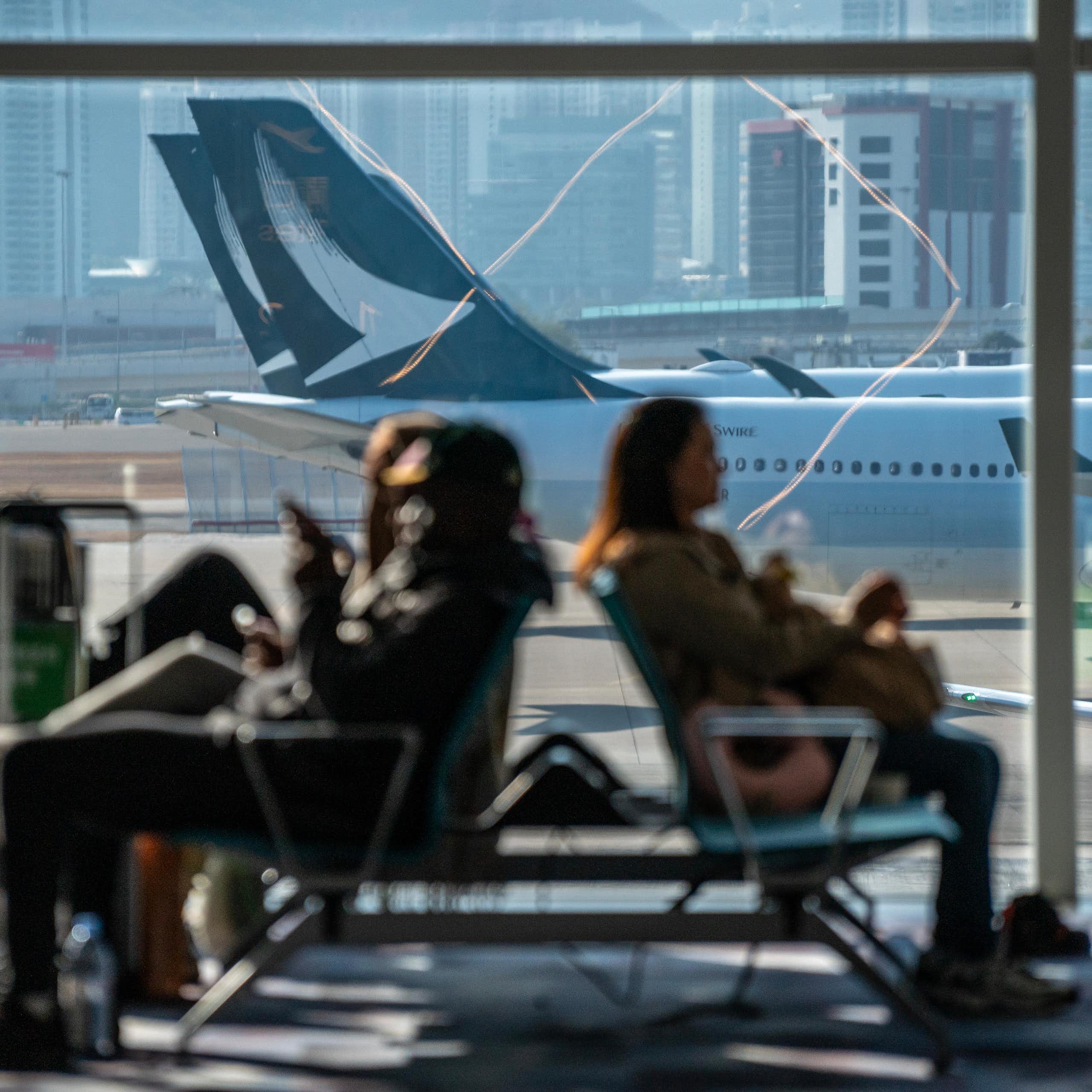 people sitting in a waiting area with jetliners visible through a large window