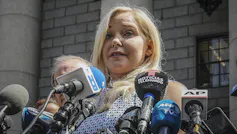 A blonde woman with a bank of microphones in front of her.