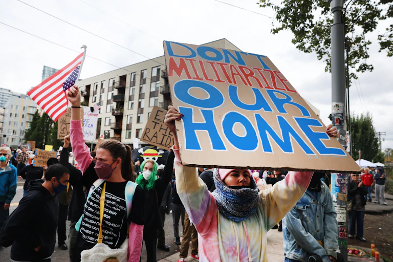 A protester with a sign 'DON'T MILITARIZE OUR HOME.'