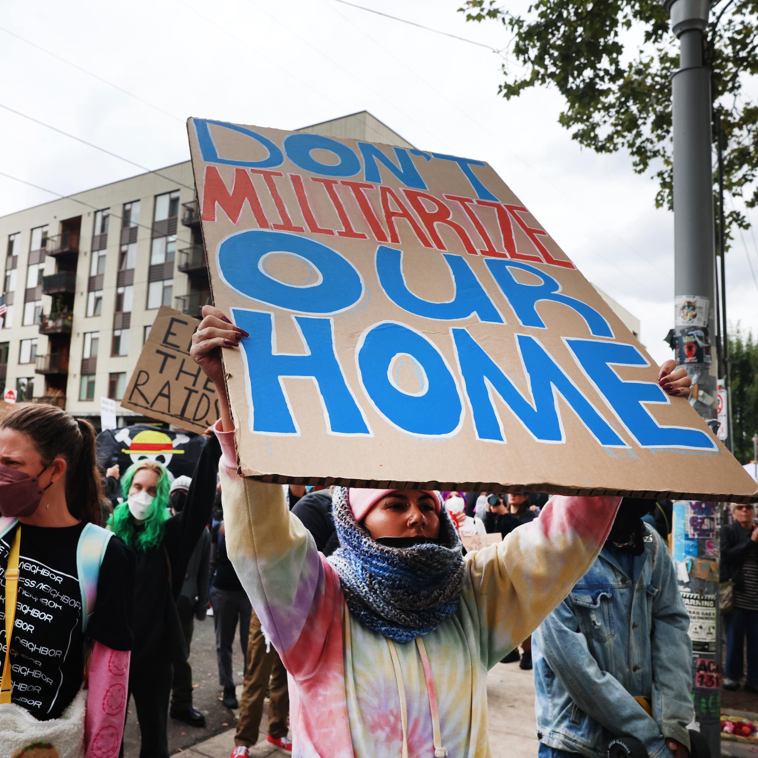 A protester with a sign 'DON'T MILITARIZE OUR HOME.'