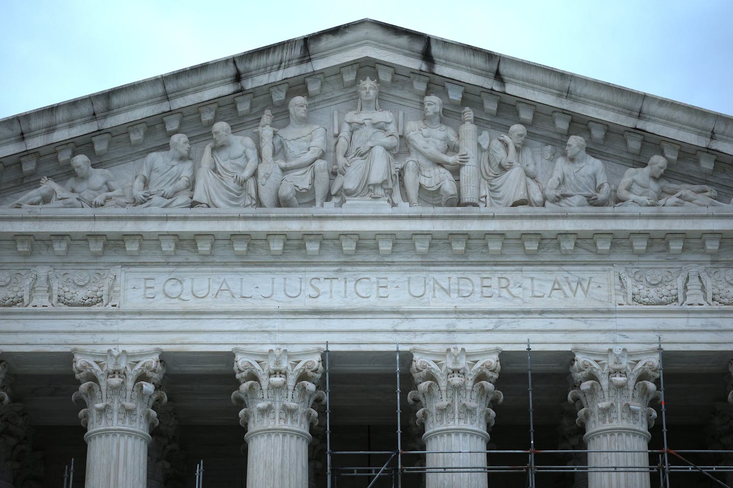 The roofline with carvings on it of a large, white, pillared building.