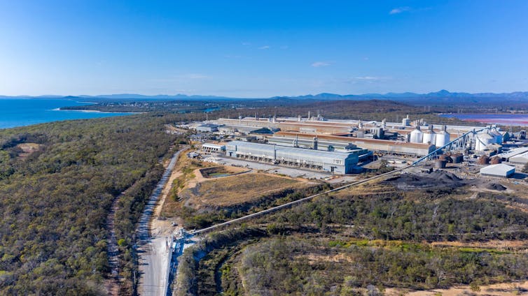 aerial view of an aluminium smelter, industrial facility surrounded by bushland and sea.