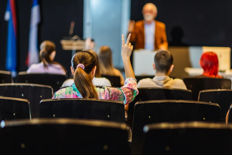 Une étudiante lève la main pour poser une question dans l'amphi d'une université.