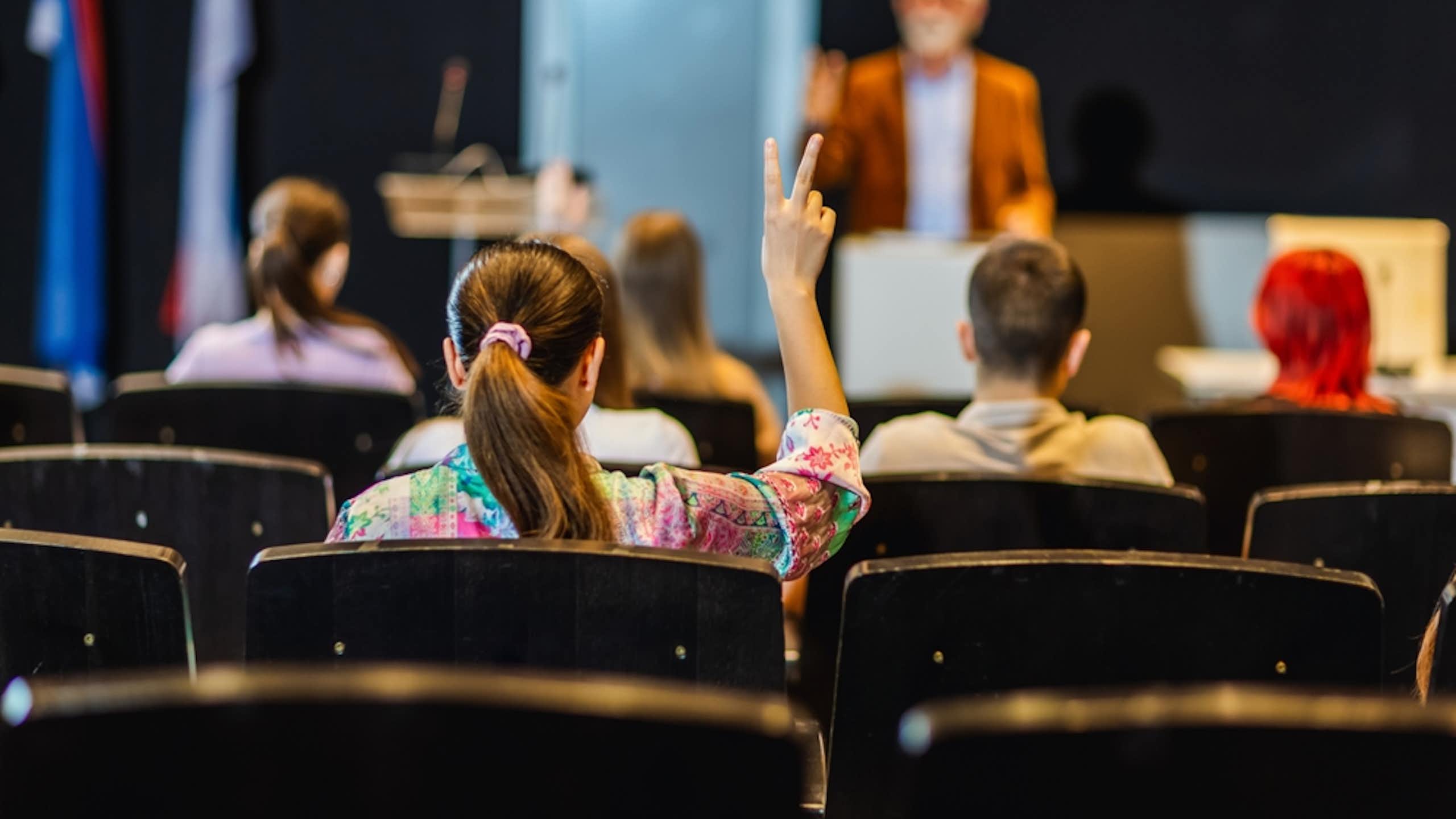 Une étudiante lève la main pour poser une question dans l'amphi d'une université.