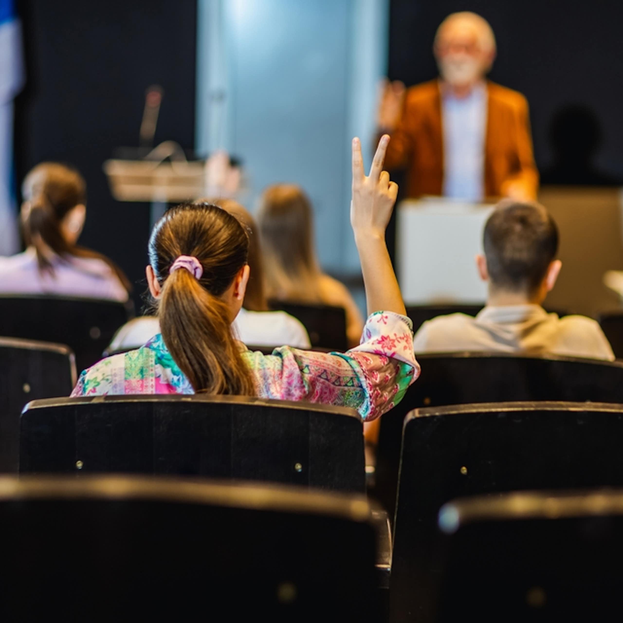 Une étudiante lève la main pour poser une question dans l'amphi d'une université.