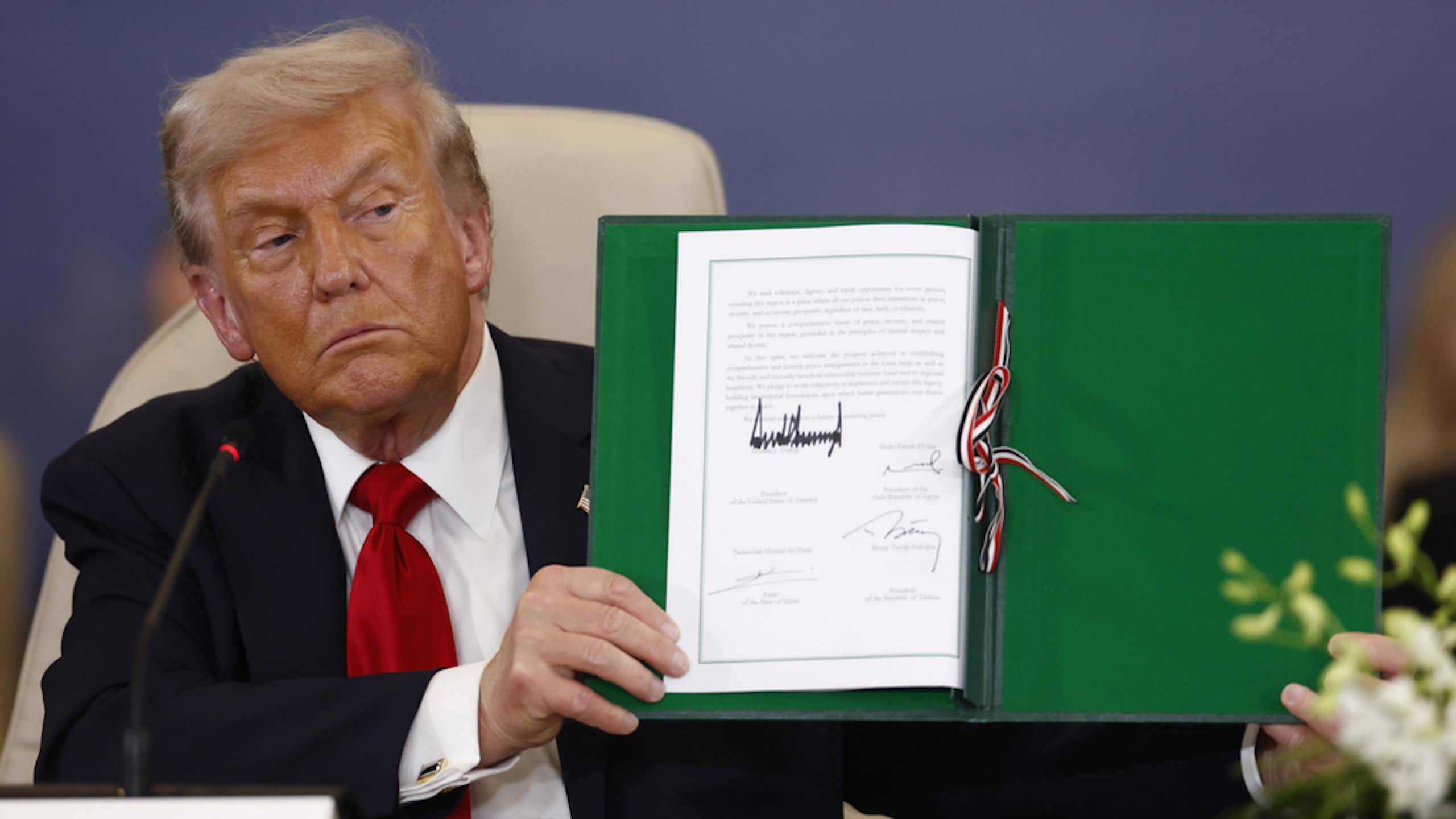 A man holds a piece of paper with a large signature.