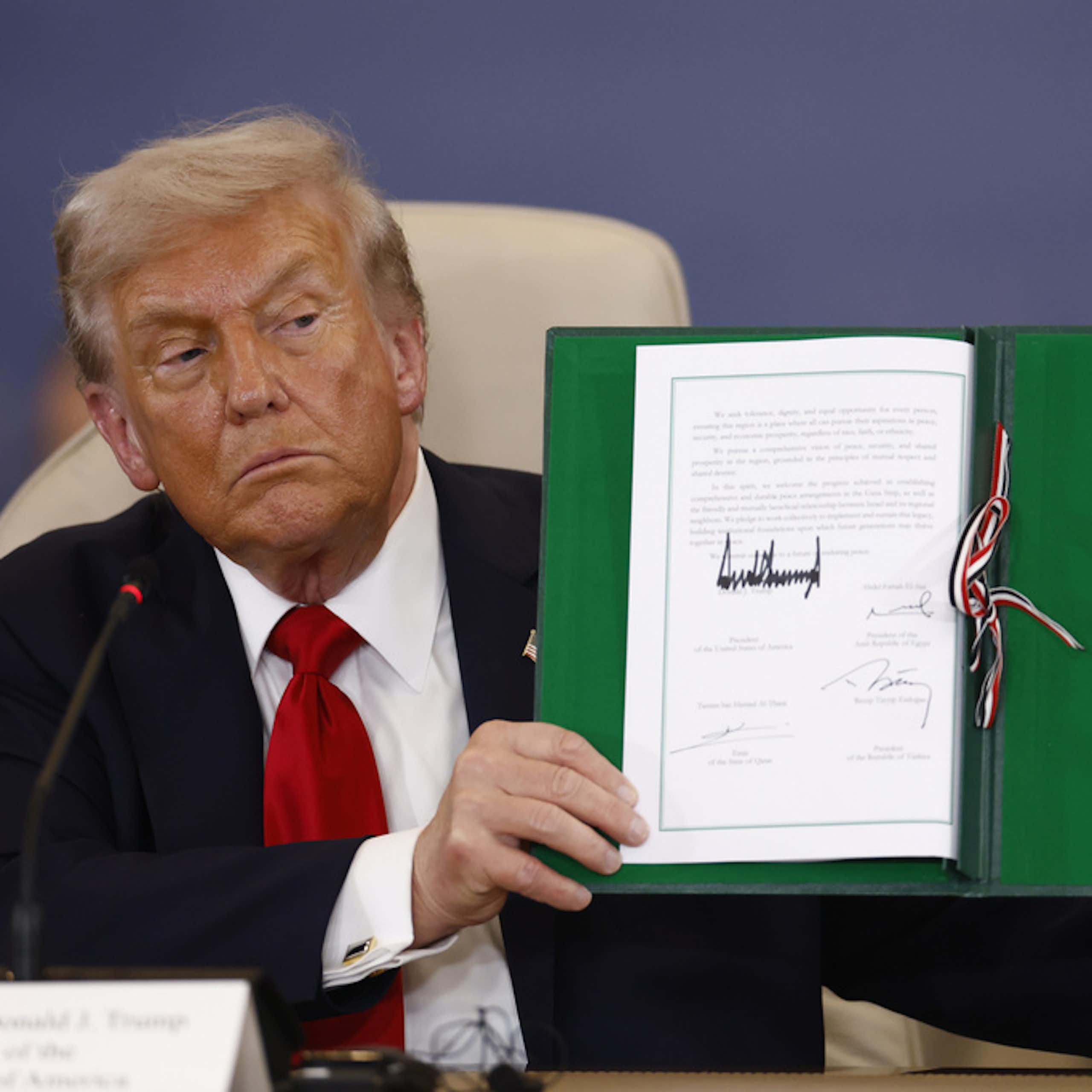 A man holds a piece of paper with a large signature.
