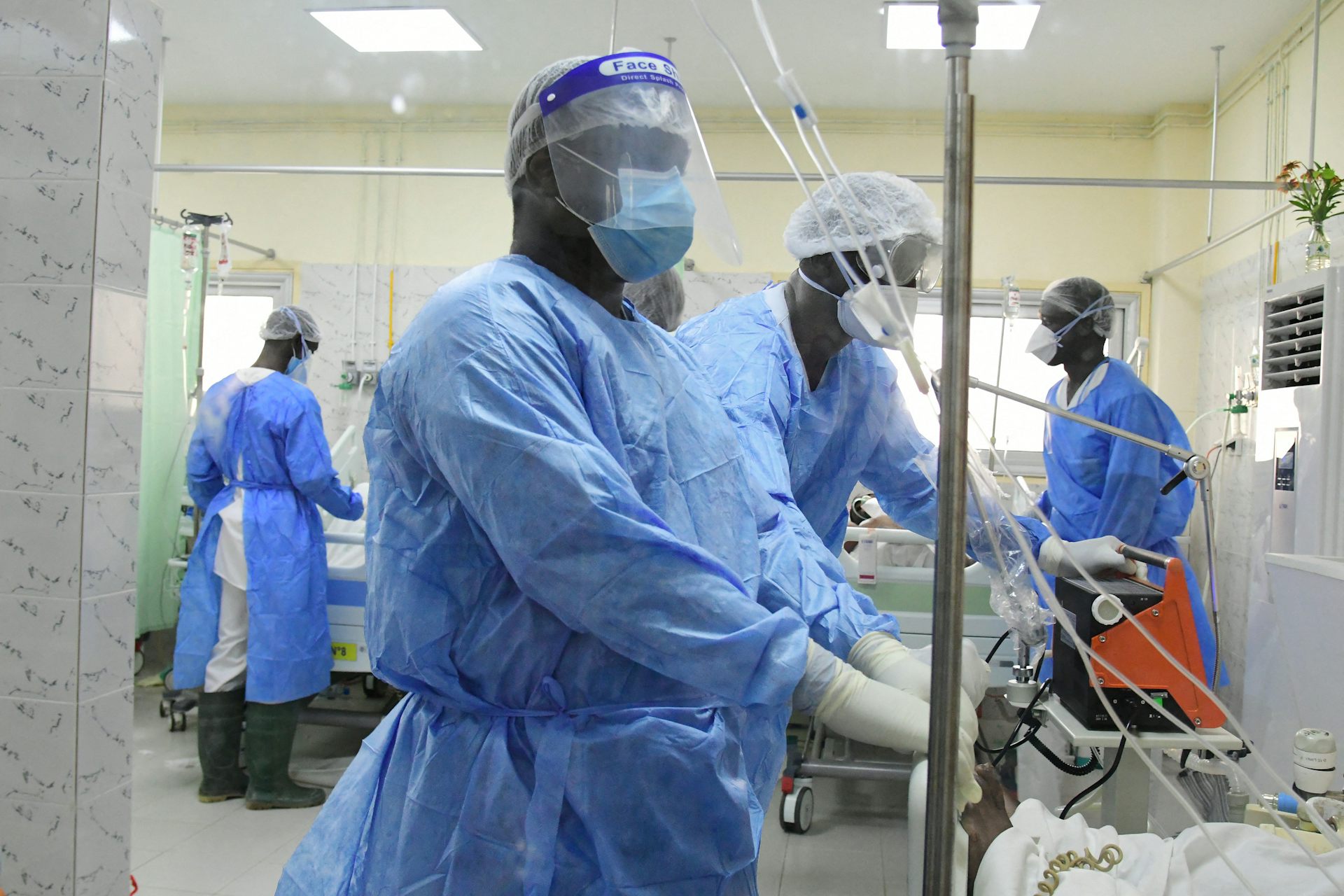 African healthcare workers in a hospital ward wearing blue clothing, face masks and gloves.