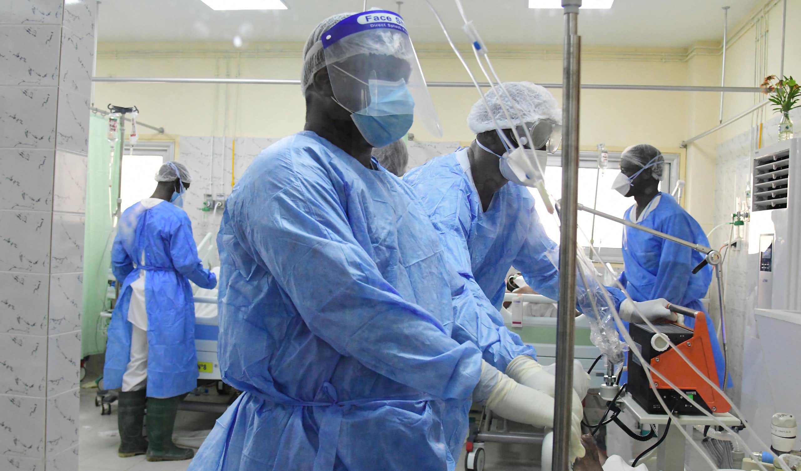 African healthcare workers in a hospital ward wearing blue clothing, face masks and gloves.