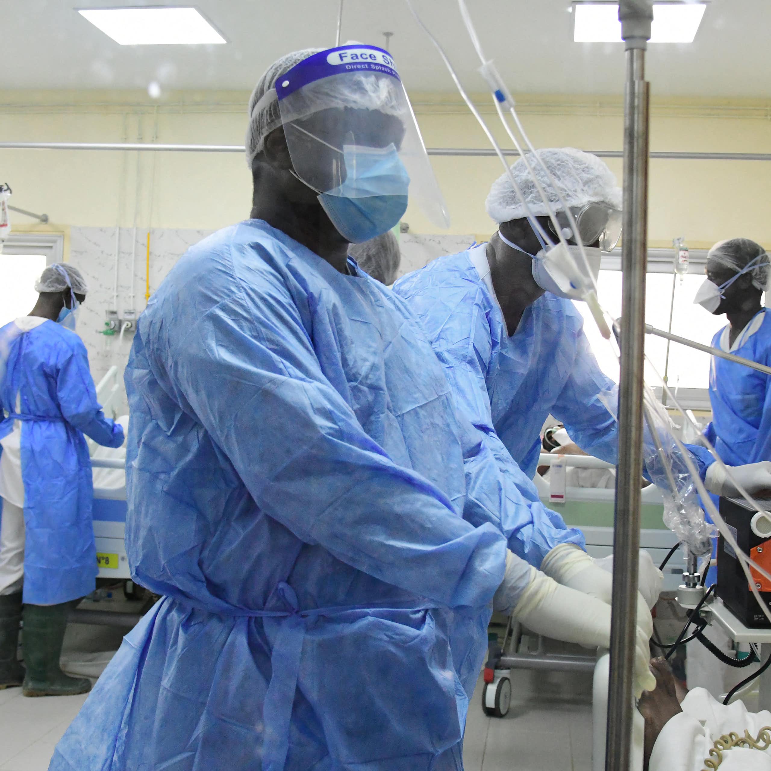 African healthcare workers in a hospital ward wearing blue clothing, face masks and gloves.