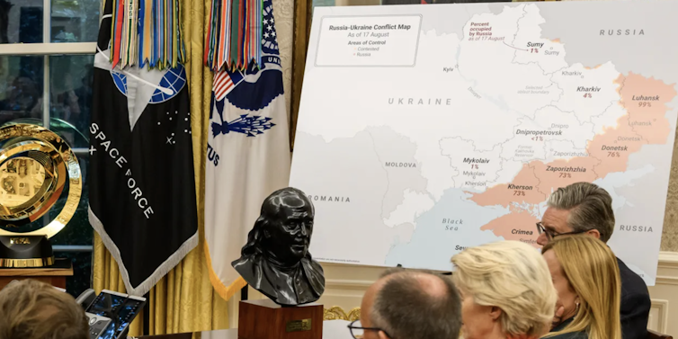 A map is shown in front of a bust and various people.