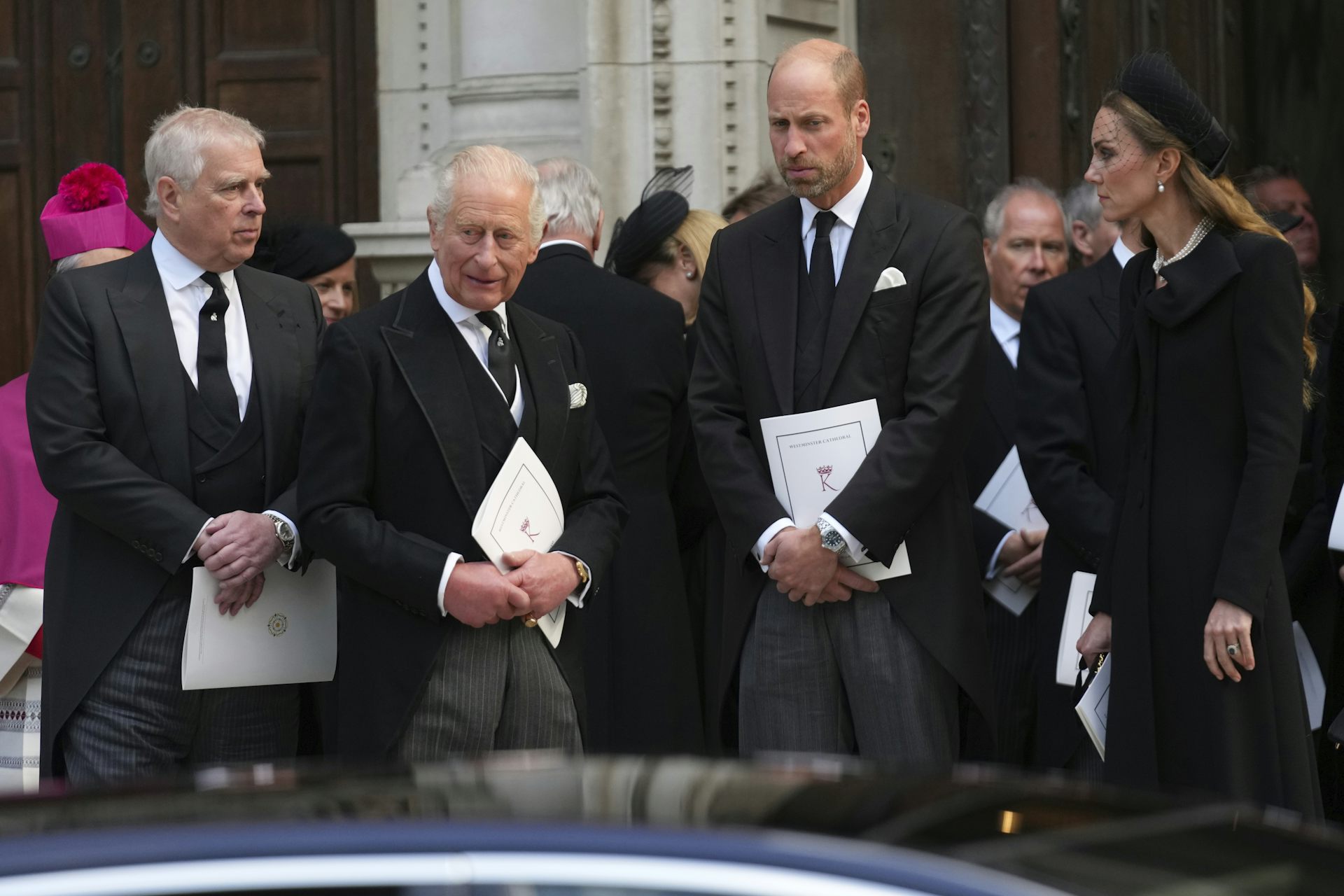 Three men and a woman dressed in black in front of a cathedral.