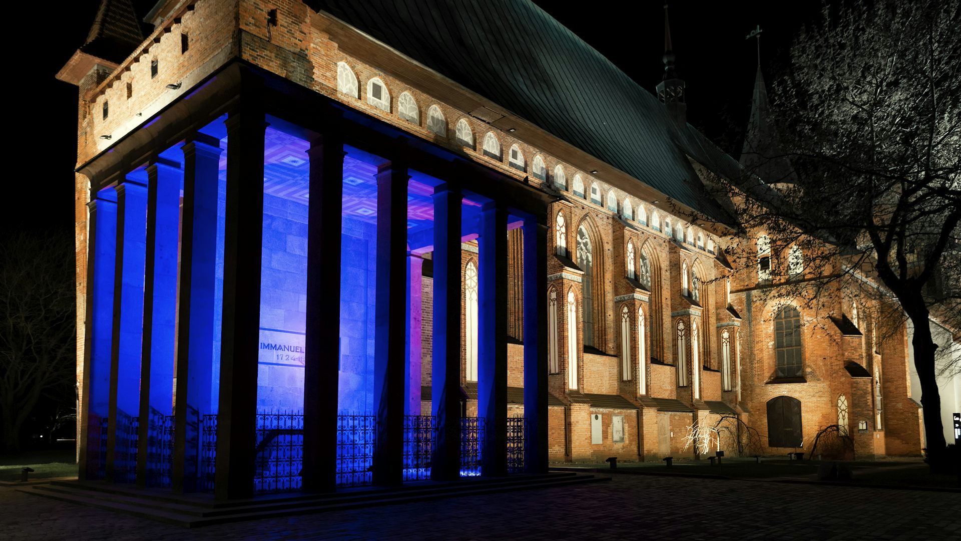 Blue neon lights illuminate a courtyard outside a large stone building, seen at night.