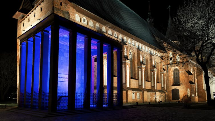 Blue neon lights illuminate a courtyard outside a large stone building, seen at night.