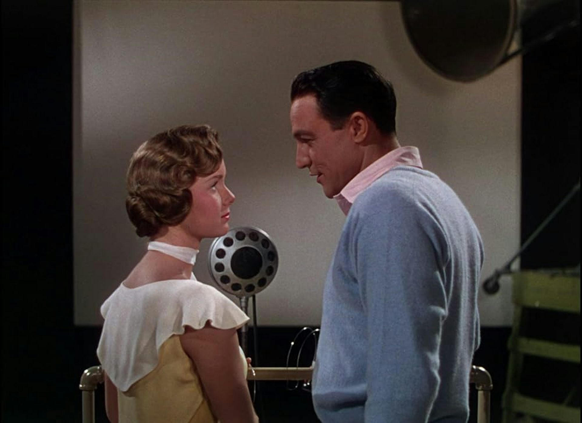 Un hombre y una mujer se miran frente a un micrófono.