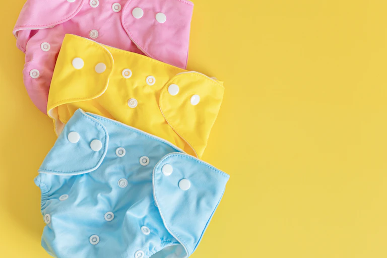 pink yellow and blue cloth nappies, flatlay on yellow background
