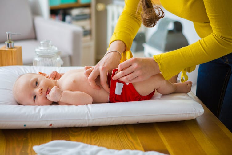 mum changing cloth nappy on baby lying on baby mat