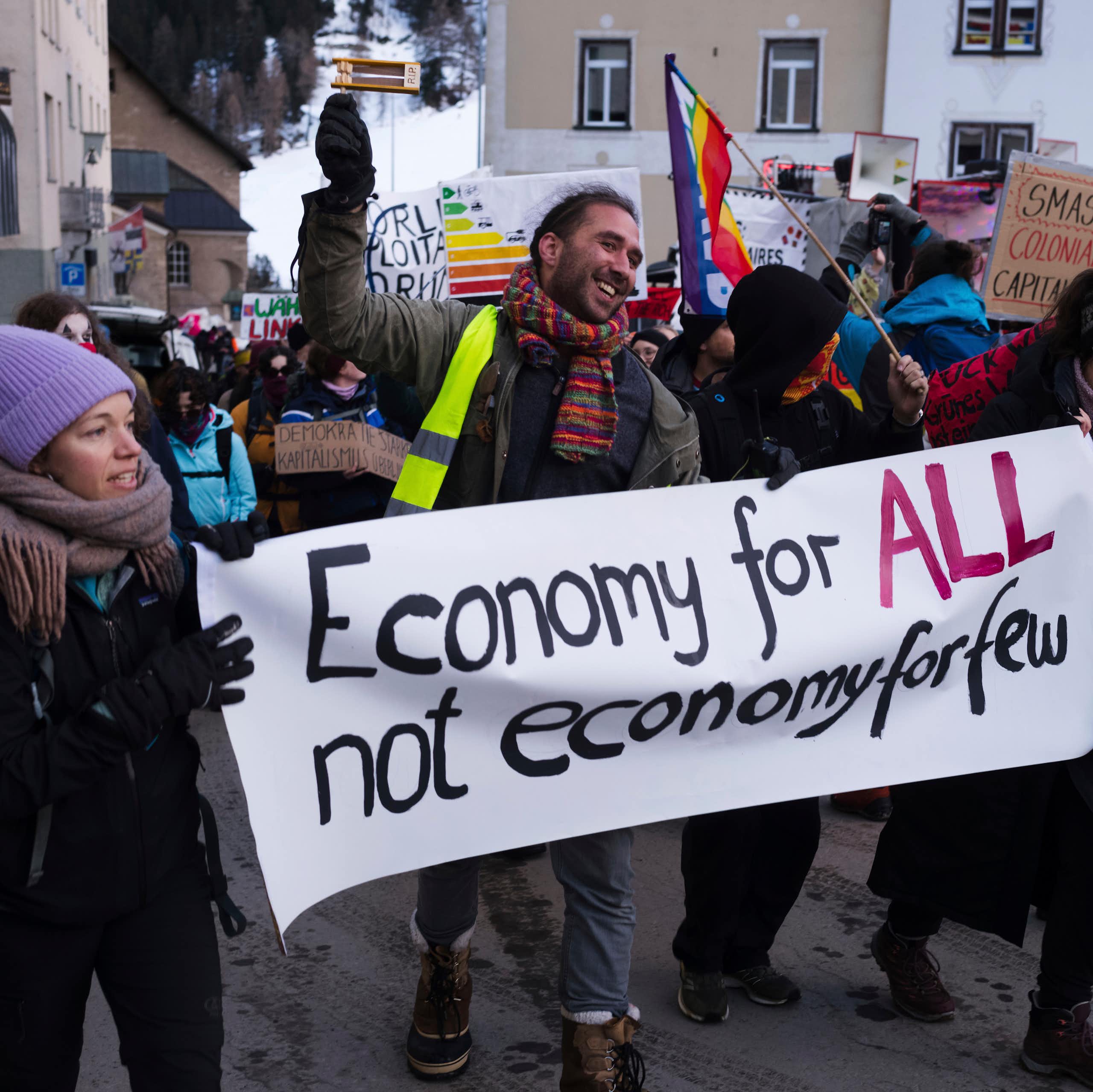 A young man and two women in winter clothing hold a sign that says, 'Economy for ALL not economy for few.'