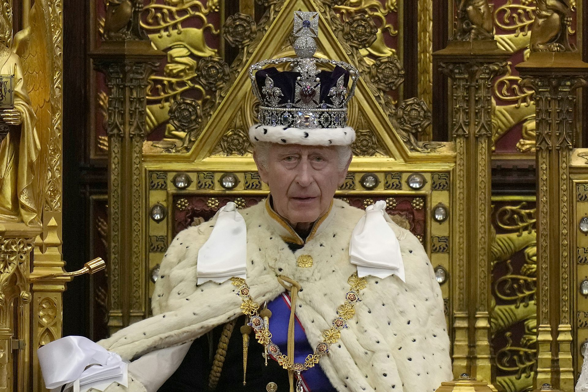 An older man in an ornate crown and robes sits on a golden throne.