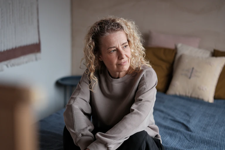 Midlife woman sits on the end of her bed