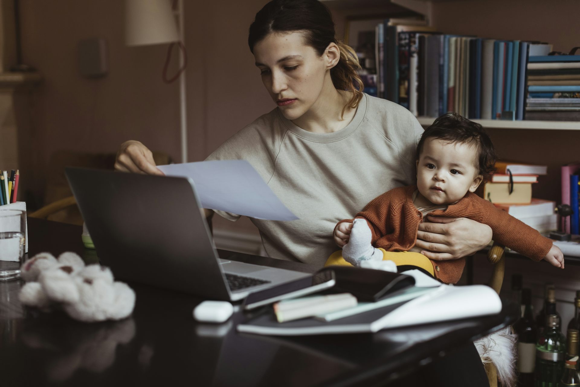 A woman holds a baby while studying a paper bill