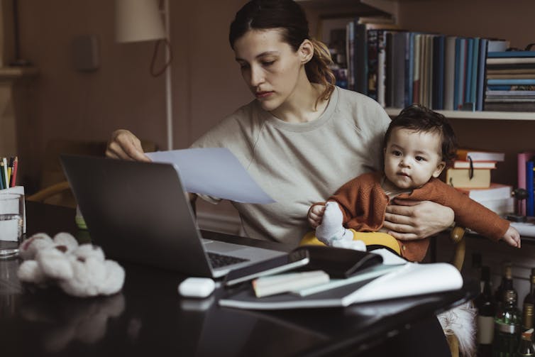 A woman holds a baby while studying a paper bill