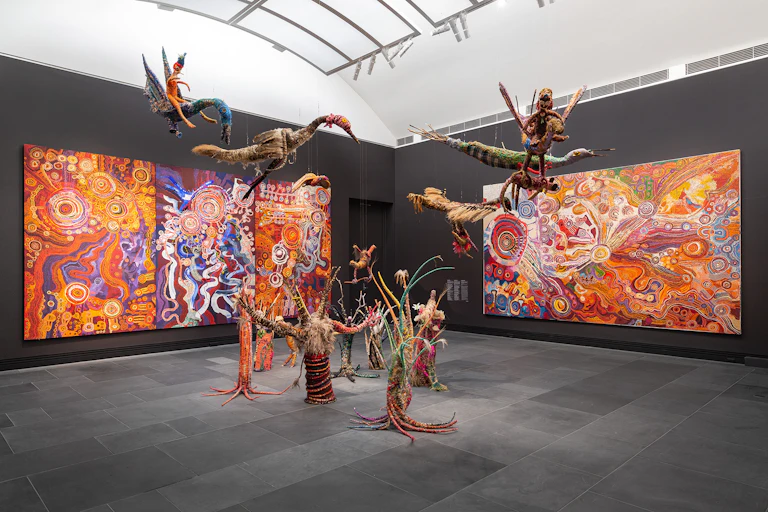 Woven creatures in front of brilliant large scale paintings.