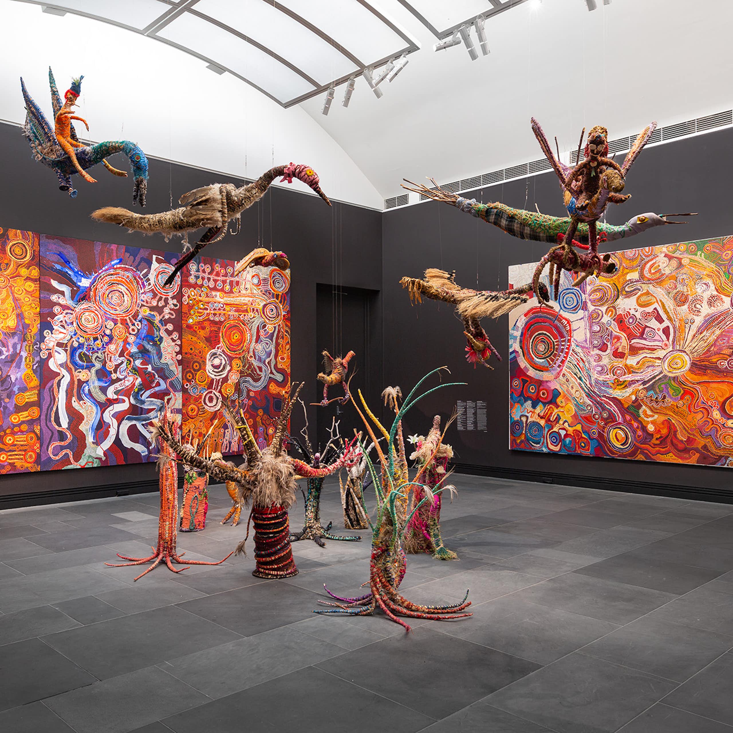 Woven creatures in front of brilliant large scale paintings.