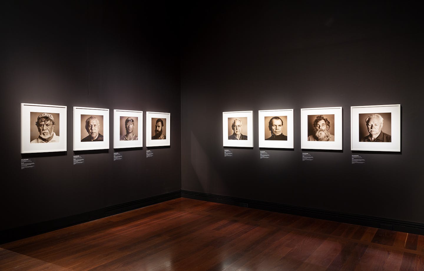 Four photographs of men hang on black walls.