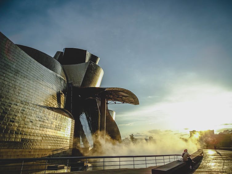 Mist rises off the river in front of a brilliant glass and metal building.