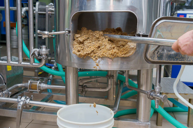 A person scrapes a sandy substance out of the door in a brewing vat