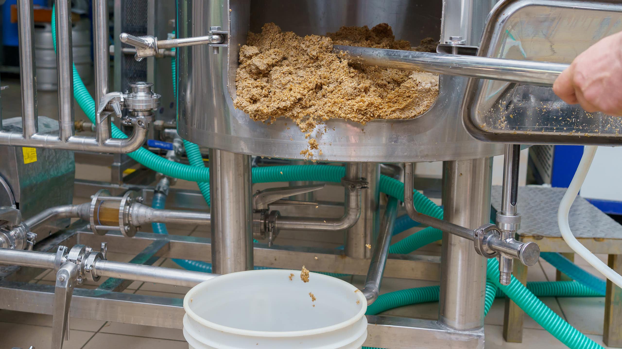 A person scrapes a sandy substance out of the door in a brewing vat