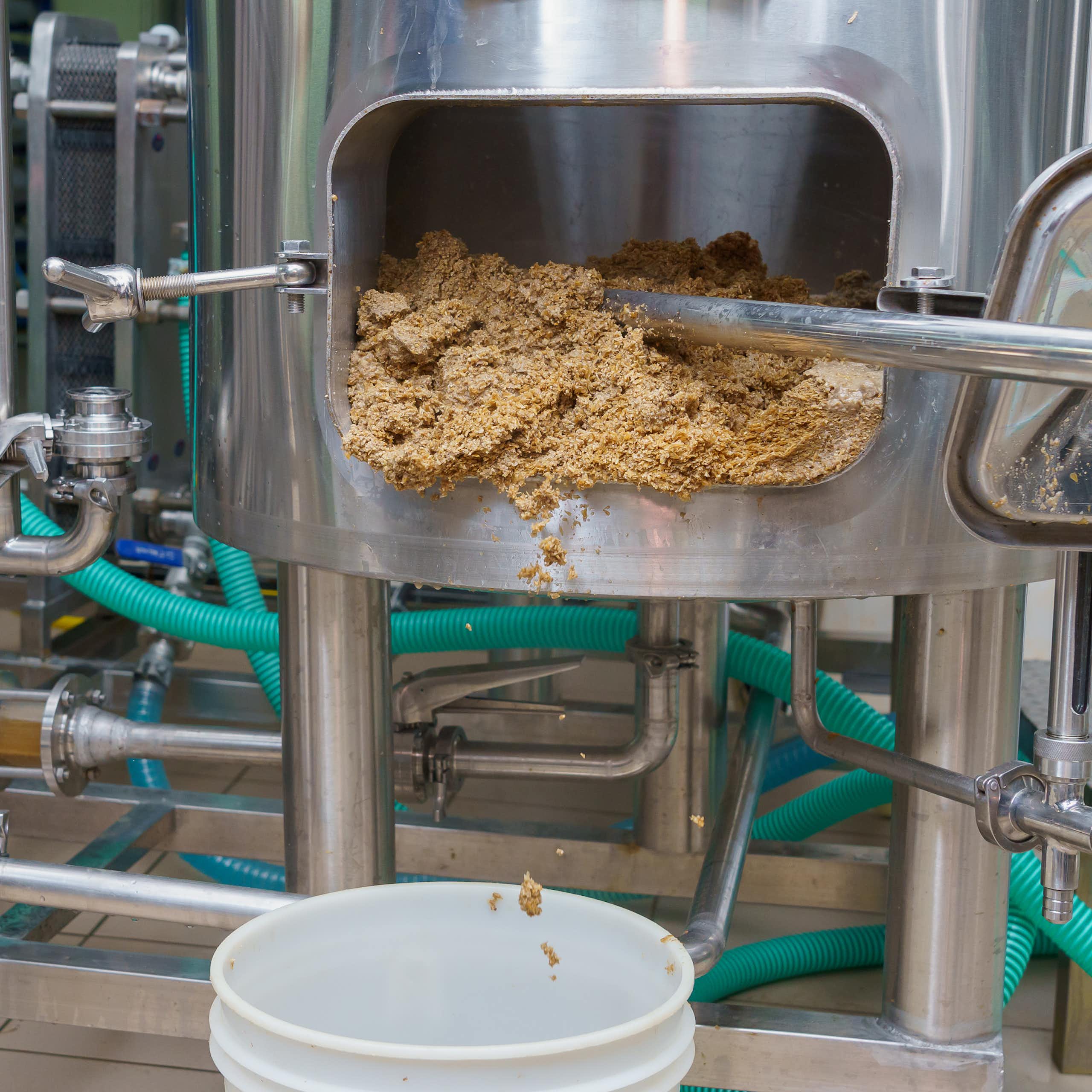 A person scrapes a sandy substance out of the door in a brewing vat