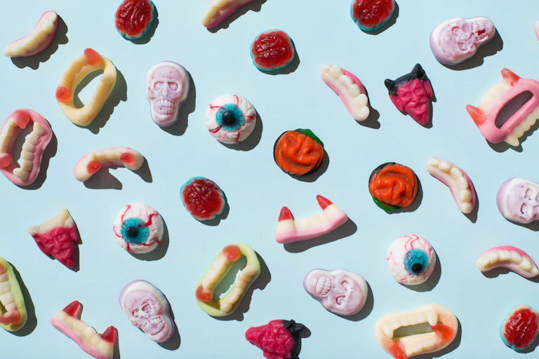Gummy lollies shaped liked eyeballs, fangs and different spooky shapes on a blue blackground.