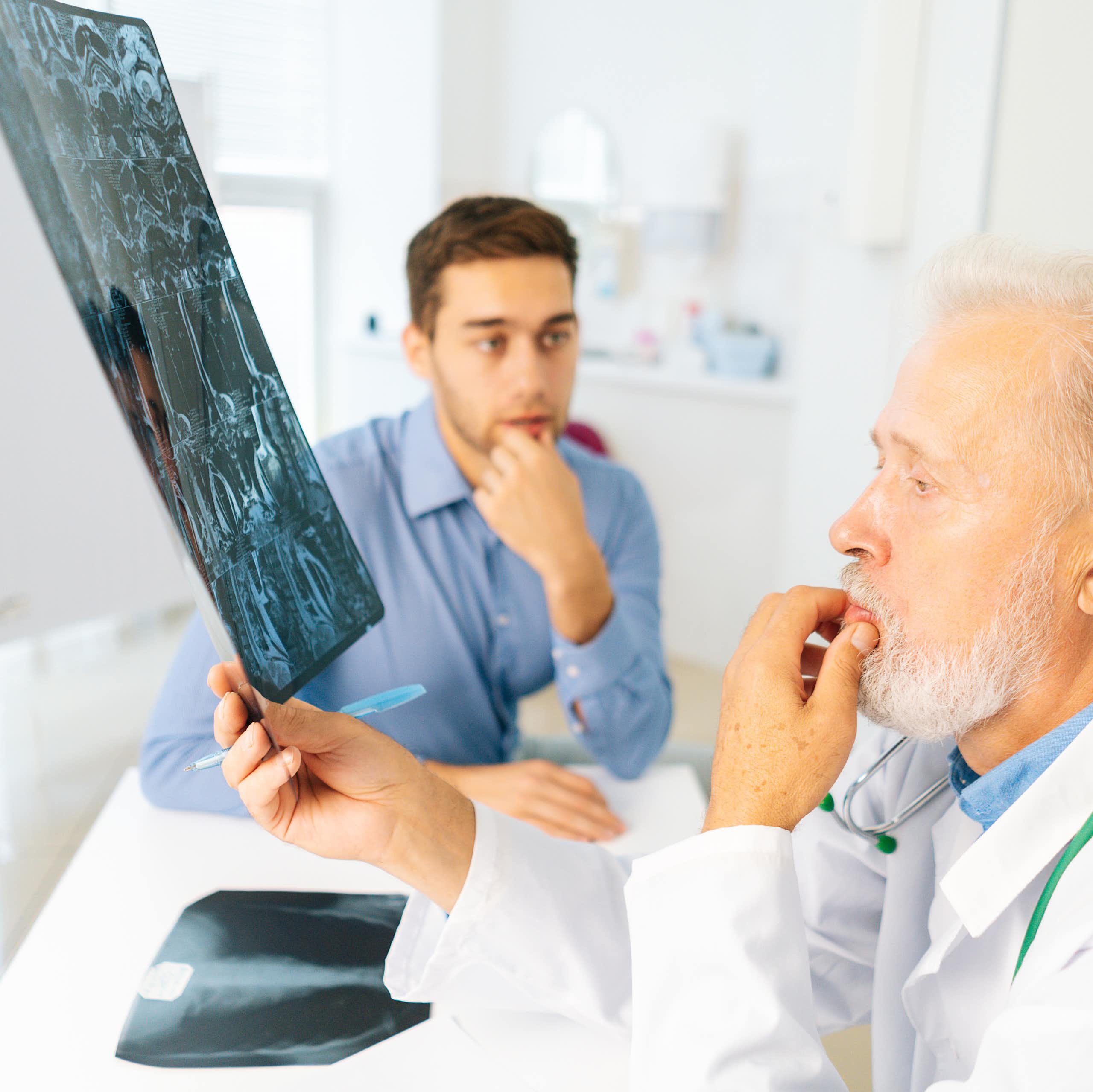 Un médico mira una radiografía de un joven (sentado al fondo con cara de preocupación).