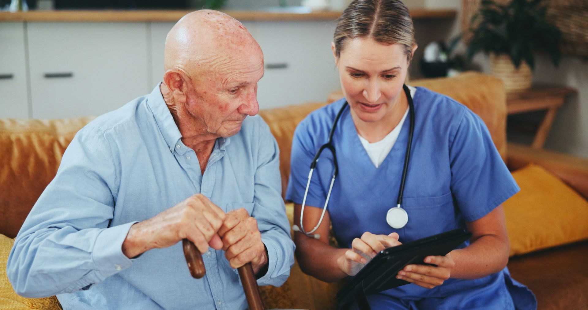 Une soignante est assise à côté d’un monsieur âgé pour des soins délivrés à son domicile