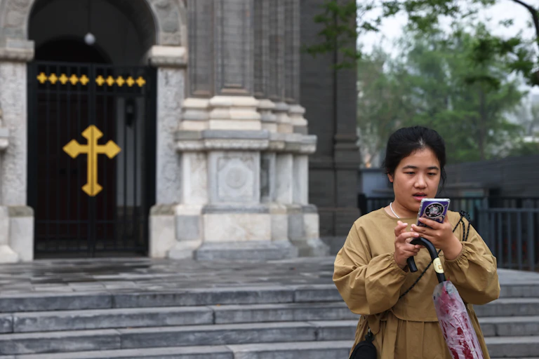 A woman stands outside a church in China, while she looks at her cellphone.