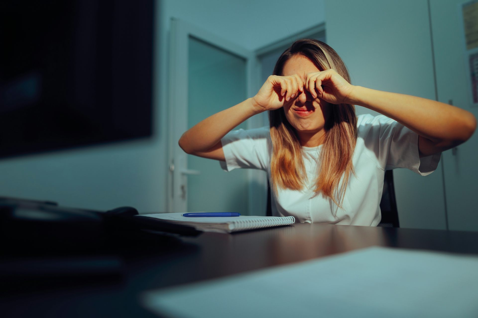 Woman set at desk rubbing her eyes.