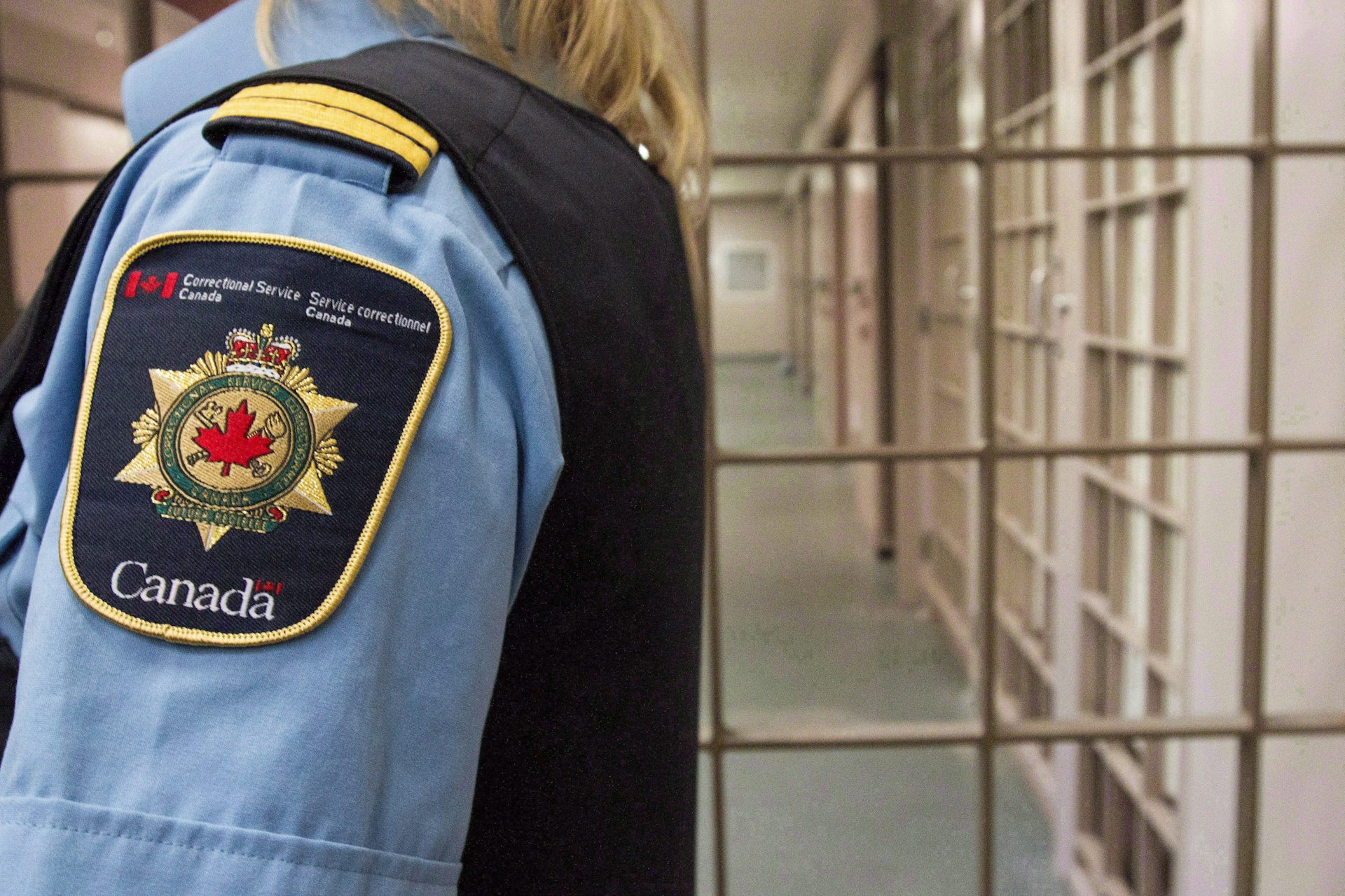 The shirt and badge of a correctional officer standing outside the bars of a prison facility.
