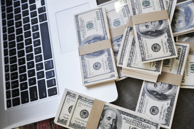 A laptop computer next to a lot of $100 bills.