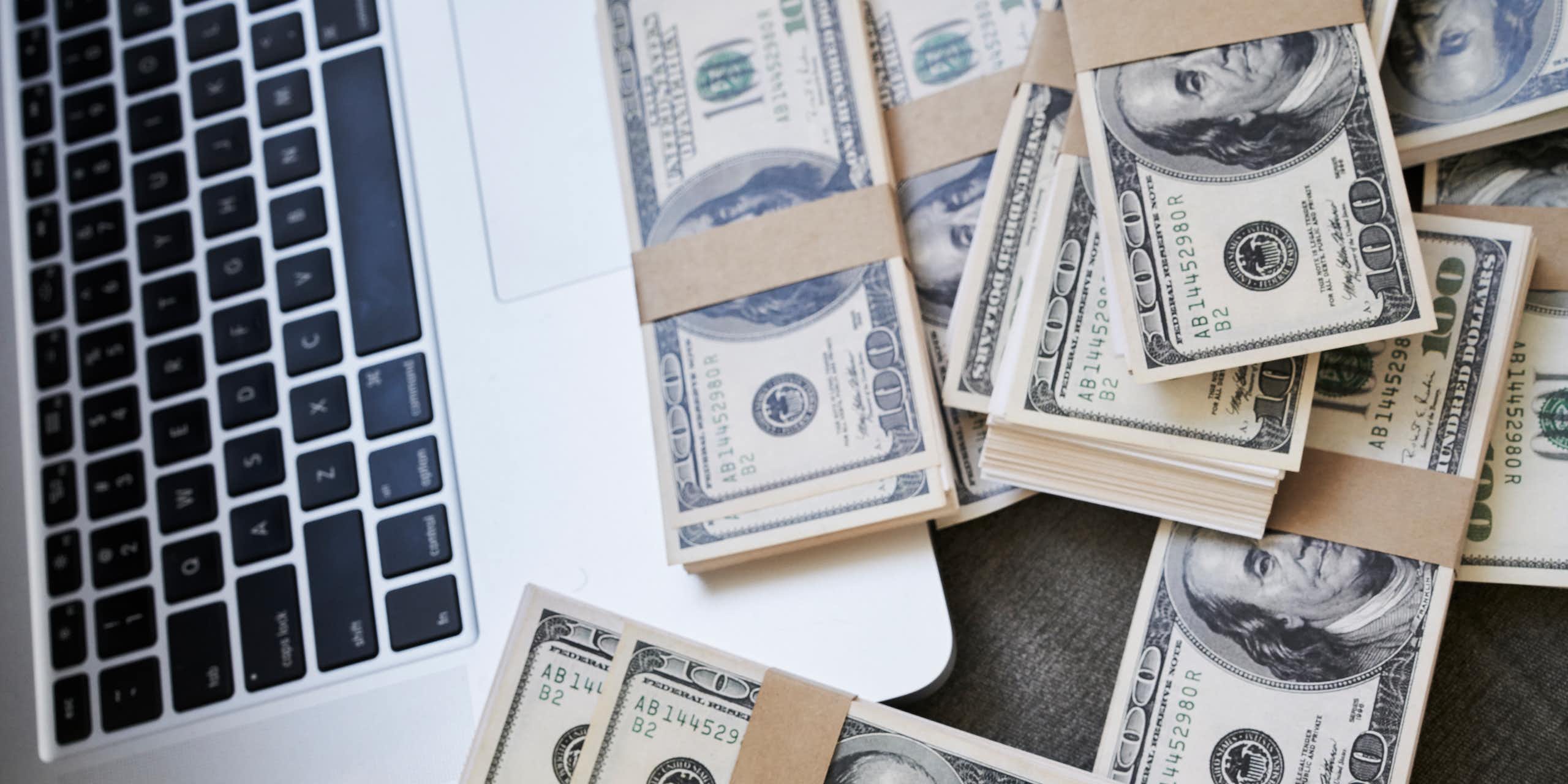 A laptop computer next to a lot of $100 bills.