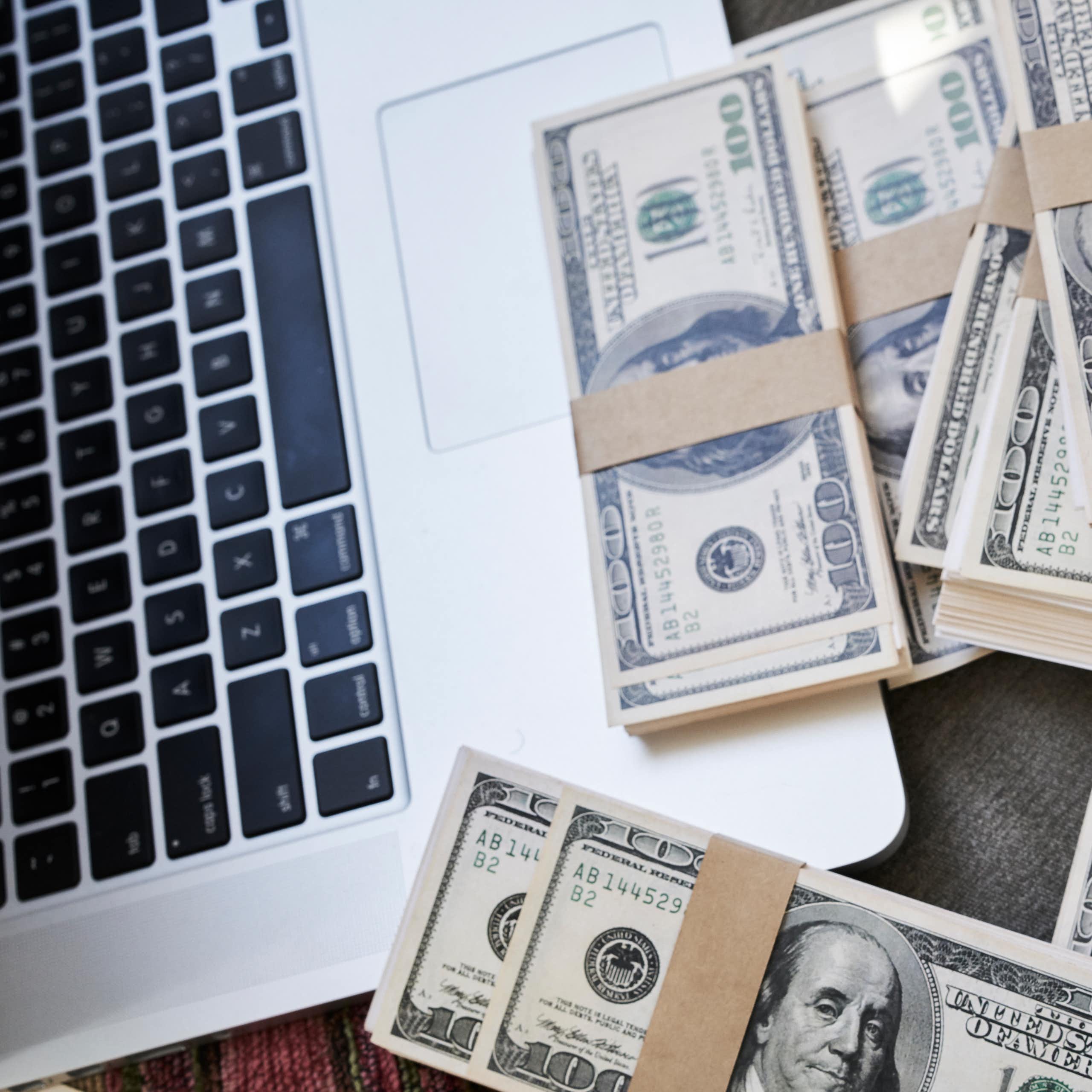 A laptop computer next to a lot of $100 bills.